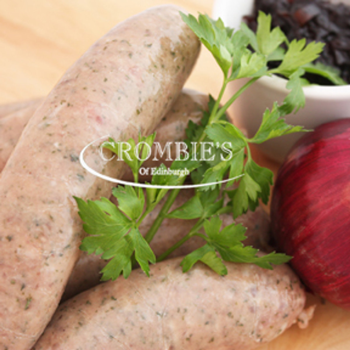 Handmade Crombies sausages dressed with fresh parsley and a tomato on a wooden board