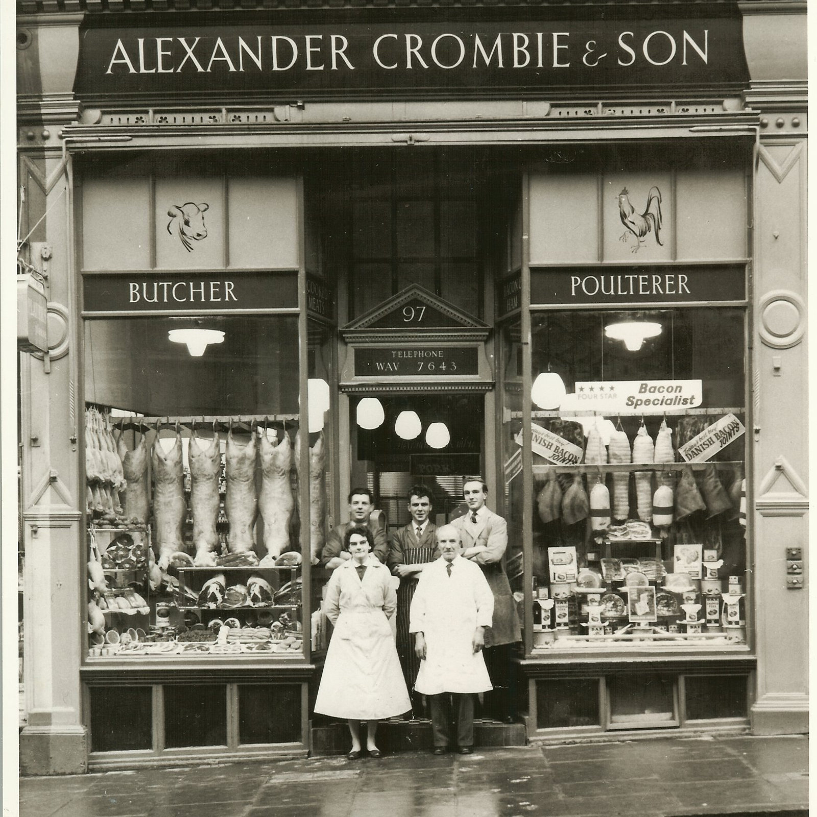 Black-and-white archive photograph of the original Crombies shopfront — a Broughton Street butcher and poulterer, staff standing at the door beneath hanging game and a bacon-specialist sign