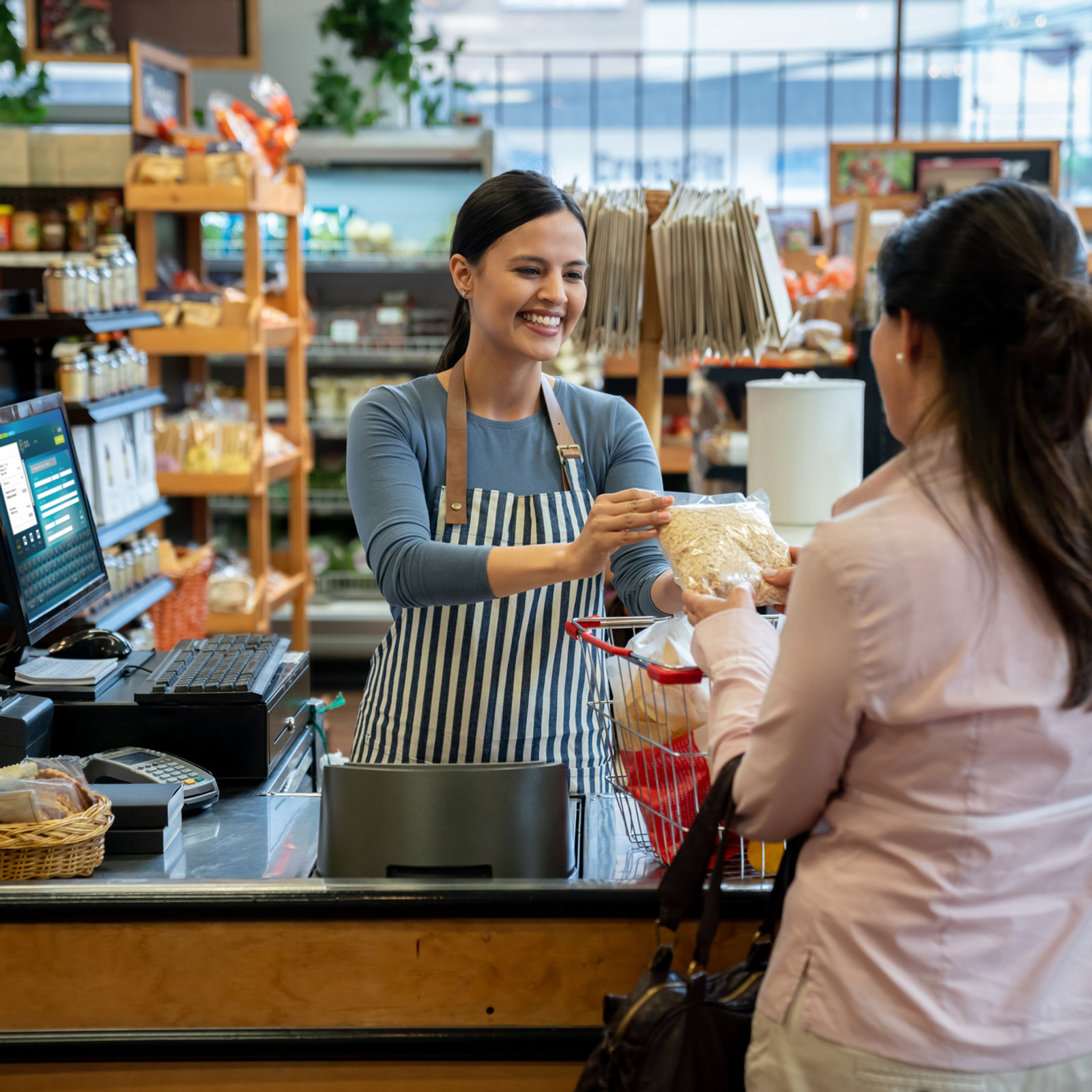 A Crombies butcher in a blue-striped apron serving a customer at the counter
